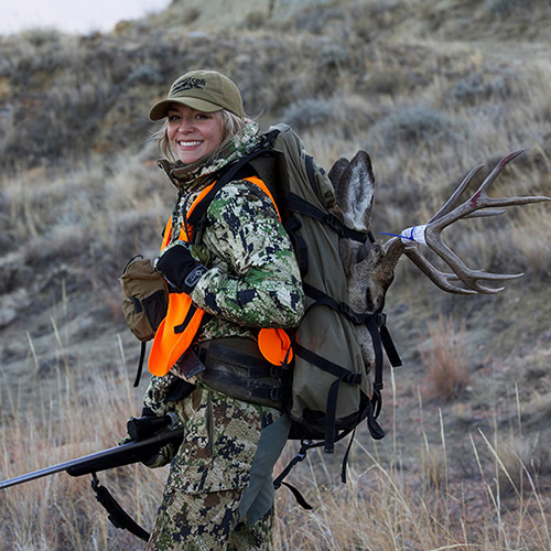 Maddie Richards in camo packing out a mule deer